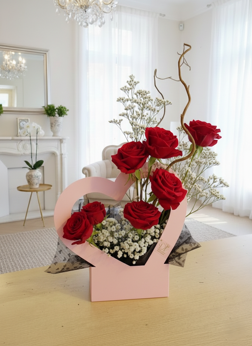 Composizione floreale di San Valentino in box rosa a forma di cuore con rose e fiori misti su tavolo in legno, stile elegante e raffinato.