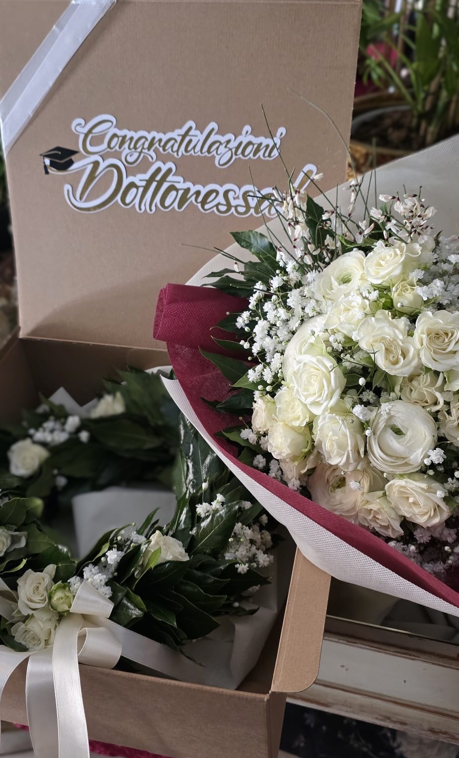 Kit Proclamazione Aura White: l'eleganza senza tempo del bianco per il tuo giorno più importante. Include corona d'alloro artigianale e bouquet coordinato, presentati in una scatola esclusiva e personalizzabile. Kit laurea Aura White: corona d'alloro con fiori bianchi e bouquet coordinato in scatola personalizzata con dedica "Congratulazioni Dottoressa" e nome esterno.