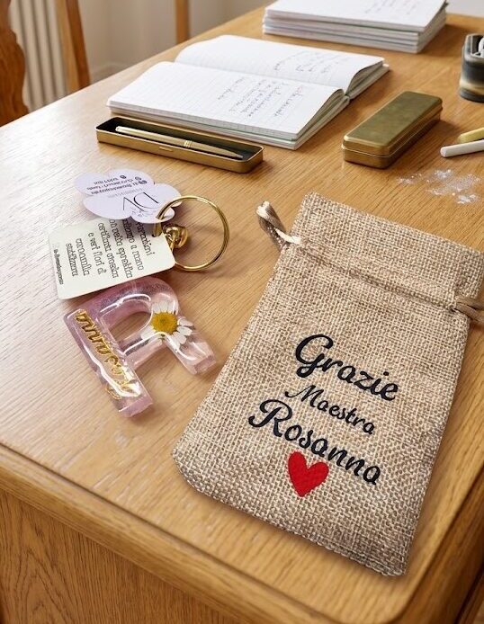 Portachiavi in resina personalizzato con lettera R e margherita su cattedra scolastica con sacchetto regalo per maestra