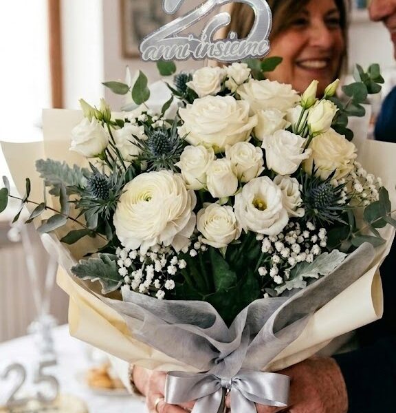 Flower Topper artigianale '25 Anni Insieme' argento olografico inserito in un bouquet di rose bianche e thistles, tenuto da una donna sorridente. Effetto finito per Nozze d'Argento dvflowers.it.